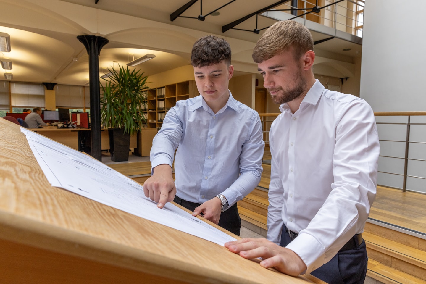 Two men review architectural plans on a drafting table.