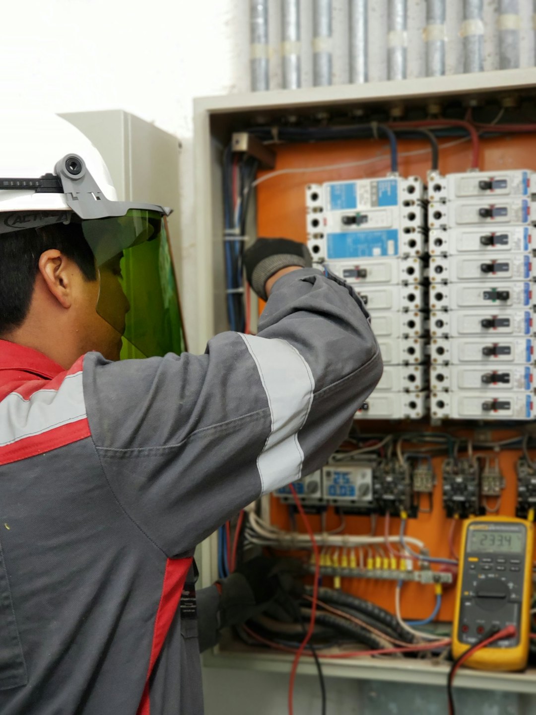 Technician inspects open electrical panel with circuit breakers and wiring.