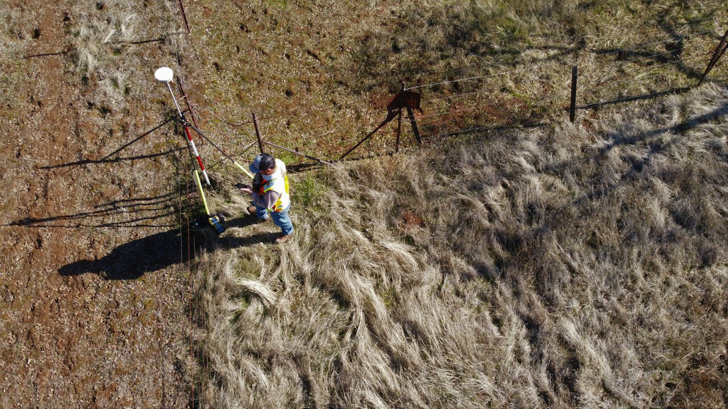 Surveyor using equipment in a dry grassy field.